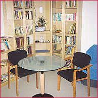 eine gemütliche Ecke mit Couch und kleinem Tischchen/Sesseln vor einem gefüllten Bücherschrank in hellem Holz gehalten